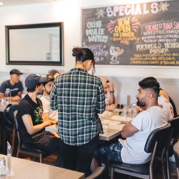 A server in a plaid shirt takes orders from customers seated at tables in Leo & Lily.