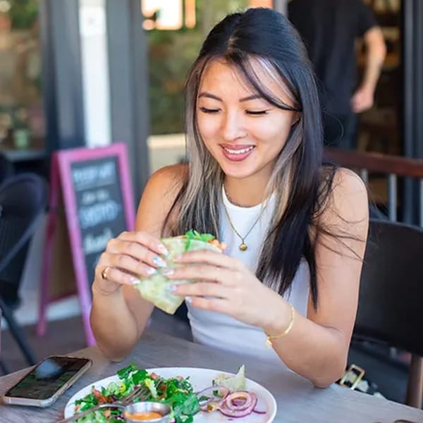 A young woman smiling while eating a lettuce wrap and salad at Leo & Lily.