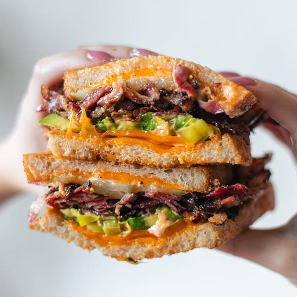 A hand holds a Leo & Lily breakfast sandwich with bacon, avocado, and melted cheese.