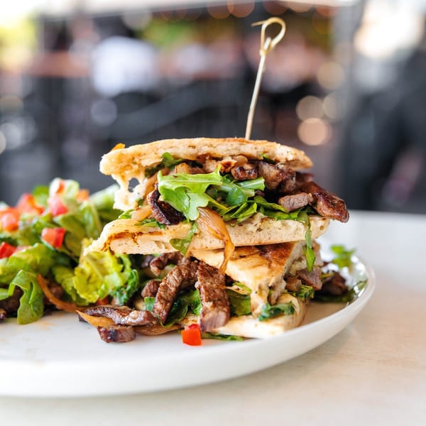 Leo & Lily's steak and arugula panini with a side salad on a white plate.