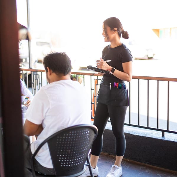 A Leo & Lily server takes an order from a customer on a sunny outdoor patio.