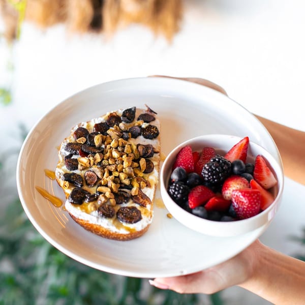 Leo & Lily's fig and granola toast with a side of fresh berries, held by hands.
