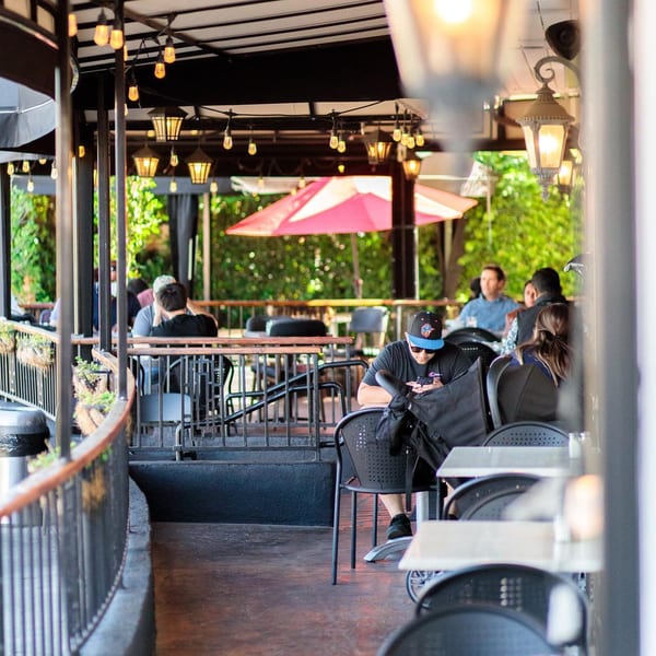 Leo & Lily's outdoor patio with string lights, a red umbrella, and blurred patrons dining.