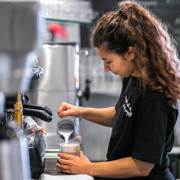 A barista at Leo & Lily pouring steamed milk into a coffee drink, creating latte art.