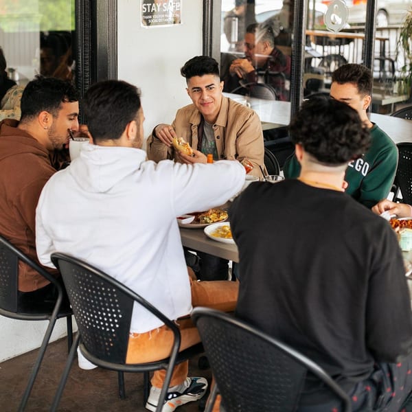 Five young men enjoying breakfast and conversation at an outdoor table at Leo & Lily.