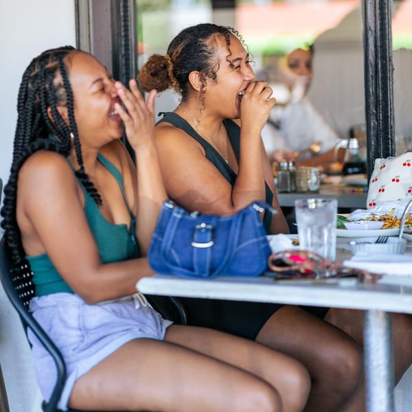 Two women laughing joyfully while dining outdoors at Leo & Lily, with breakfast dishes on the table.