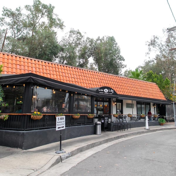 Exterior of Leo & Lily restaurant with a red tile roof, black awning, and outdoor patio seating.