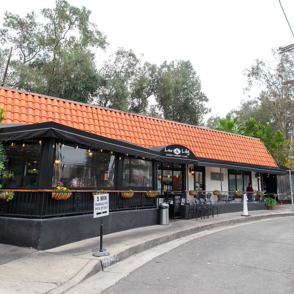 Exterior of Leo & Lily restaurant with a red tile roof, black awning, and outdoor patio seating.