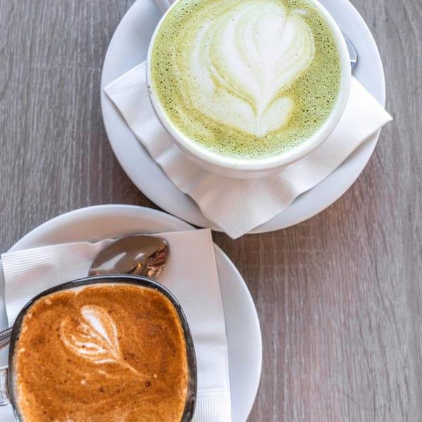 Overhead view of a green matcha latte and a brown coffee drink, both with heart-shaped latte art.