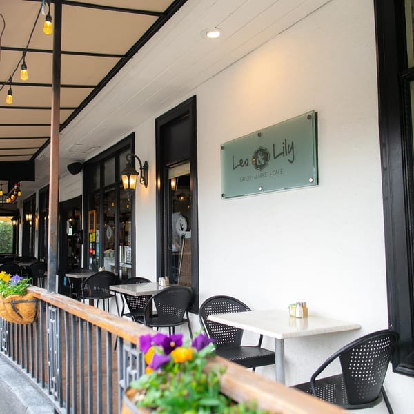 Outdoor patio seating at Leo & Lily restaurant with black chairs, white tables, and string lights.